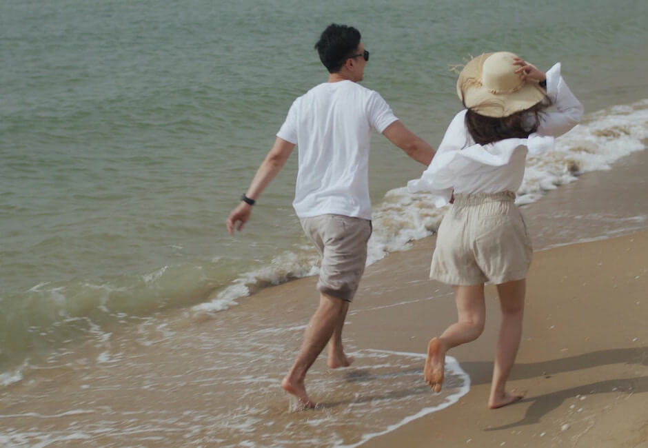 浜辺を手を繋いで散歩する男女カップル