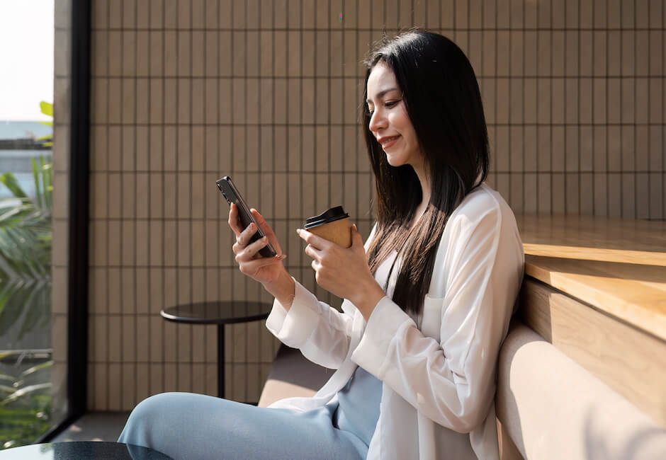コーヒーを片手にスマホ画面を見つめる女性